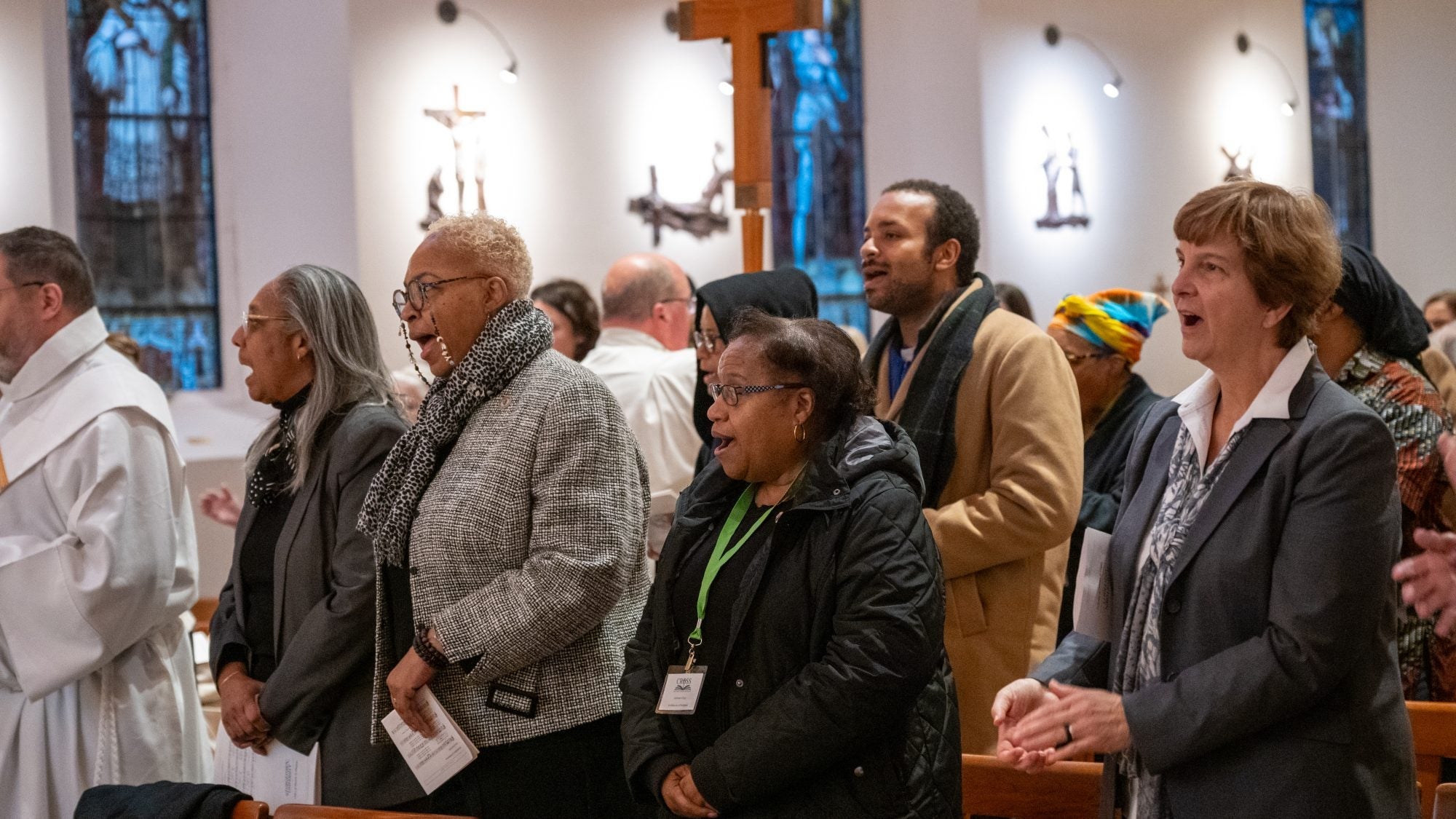 A mixed group of people standing and singing at the pews in Dahlgren Chapel.