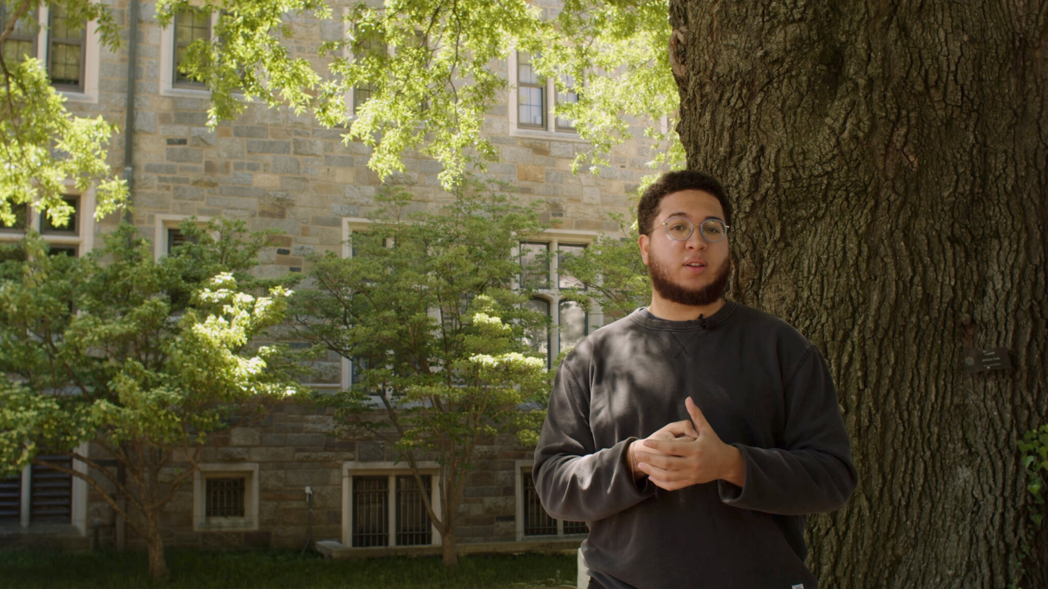 A man stands outside in front of a large tree trunk.