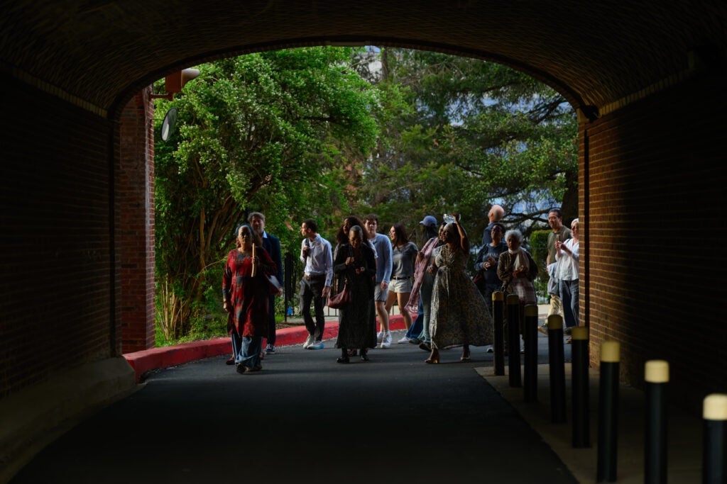 A large group of people walk through an outdoor brick archway.